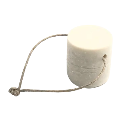 Un détachant solide pour le linge sous forme de cylindre blanc, accompagné d'une corde en fibre naturelle qui semble servir de manche ou de support pour le produit.